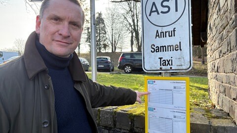 Ortsbürgermeister Torsten Müller zeigt auf den Busfahrplan von Ockenfels