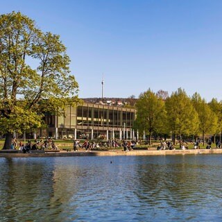 Menschen vor dem Landtag in Stuttgart, dem Zentrum der BW-Politik, im Vordergrund der Eckensee.