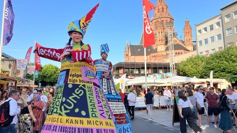 Straßenszene mit farbenprächtig kostümierten Artisten auf Stelzen während der Johannisnacht in Mainz 