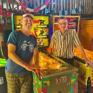 Peter Stadtlmaier und Peter Löffler vor einem Flipperautomat in der Scheune in ihrem Flippermuseum in Pliezhausen-Gniebel. Hier gibt es auch noch viele andere Spielautomaten.
