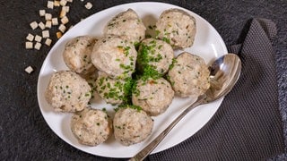 Ein weißer Teller voller Knödel mit Pfälzer Leberwurst. An der Seite des Tellers liegt ein Servierlöffel.