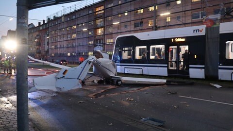 Das Wrack eines Leichtflugzeugs liegt mitten auf einer befahrenen Straße. Im Hintergrund die Stadtbahn.