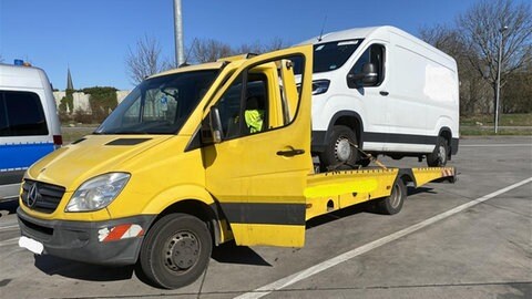 Ein Autotransporter steht mit einem geladenen Kleintransporter auf einem Parkplatz.