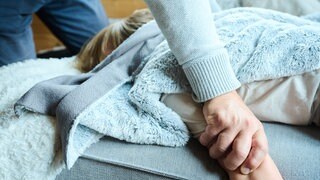 Symbolbild: Eine erwachsene Person greift ein Kind fest am Arm, während es auf einer Couch liegt.