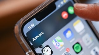 Eine Hand hält ein Smartphone, auf dem ein anonymer Anrufer angezeigt wird. | So echt kann ein Schockanruf mit KI-Stimme klingen