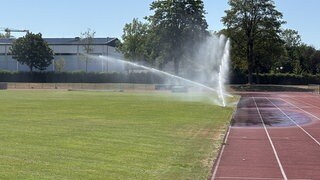 Ein Sportplatz, auf dem zwei Rasensprenger laufen. Die Stadt Neu-Ulm bewässert bei großer Hitze ihre Sportplätze täglich und stundenlang.
