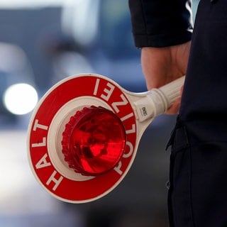 Ein Polizist hält eine Anhaltekelle in der Hand.