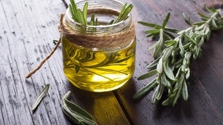 Kleines Glas befüllt mit Öl und Rosmarin. Rosmarin ist nicht nur beliebt als Gewürz, sondern ein bewährtes Naturheilmittel in der Medizin. Wertvolle Inhaltsstoffe wirken belebend, helfen bei Neurodermitis und niedrigem Blutdruck.