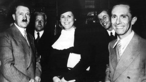 Historische Schwarz-Weiß-Aufnahme eines Empfangs im Haus Wahnfried in Bayreuth. Zu sehen sind unter anderem Adolf Hitler, Dirigent Franz von Hoesslin, Sängerin Maria Müller und Joseph Goebbels neben Winifred Wagner. Die Aufnahme zeigt die Verflechtung der Bayreuther Festspiele mit dem Nationalsozialismus.
