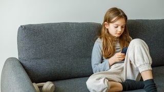 Ein Mädchen sitzt auf dem Sofa mit einem Smartphone. Digitale Endgeräte, Social Media und Künstliche Intelligenz bergen viele Gefahren, besonders für Kinder und Jugendliche (Symbolbild).