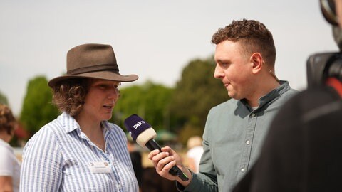 Ein Reporter interviewt eine Frau mit Cowboyhut.