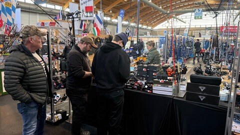 Menschen stehen in einer Messehalle um einen Stand mit Angeln