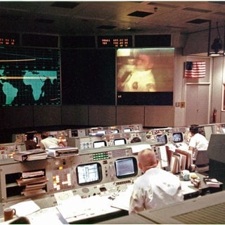 Gene Kranz (im Vordergrund mit dem Rücken zur Kamera), ein Flugdirektor von Apollo 13, beobachtet den Apollo-13-Astronauten und Piloten der Mondlandefähre Fred Haise während der vierten Fernsehübertragung der Mission am Abend des 13. April 1970 auf dem Bildschirm im Mission Operations Control Room. Kurz Nach der Übertragung ereignete sich eine Explosion, die jede Hoffnung auf eine Mondlandung zunichte machte und das Leben der Besatzung gefährdete.