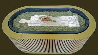 Heu, Stroh, Blumen und eine Holzfigur liegen in einem sogenannten „Kokon“ bei einem Pressegespräch zu der neuen Bestattungsform "Reerdigung" in der Kapelle auf dem Parkfriedhof Eichhof. Der Anbieter „Meine Erde“ bietet die neuen Bestattungsform an. Ein Leichnam wird auf Heu, Stroh und Grünschnitt gebettet, innerhalb von 40 Tagen wird er zu Erde.