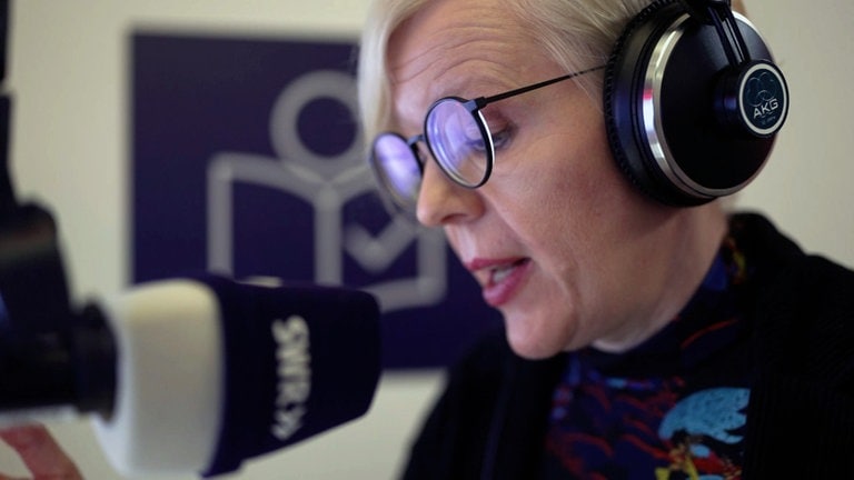Das Bild zeigt eine blonde Sprecherin mit Kopfhörern an einem SWR Mikrofon