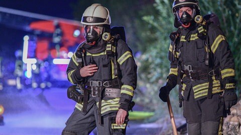 Feuerwehrleute stehen im Dunklen vor einem Löschwagen (Symbol). Feuerwehrleute (Symbol). Bei der Berufsfeuerwehr Mainz ist es nun möglich eine Ausbildung zu machen ohne vorher eine Berufsausbildung abgeschlossen zu haben. 