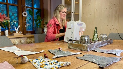 Manuela Lang sitzt an ihrer Nähmaschine, auf dem Tisch sind Hühnerpullis ausgebreitet. Sie sollen gerettete Legehennen wärmen.