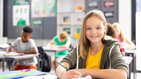 Schülerin arbeitet in der Klasse und lächelt: In Deutschland fehlt eine systematische Datenerhebung, um die Leistungen von Kindern und Jugendlichen wirklich zu verbessern. Gute, individuell erhobene und vernetzte Daten könnten die Leistungen von Schülern verbessern. Kanada oder Estland könnten Vorbild sein.