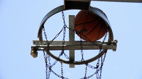 Ein kreuzförmiges Stück aus Metall liegt auf einem Basketballkorb. Der Ball kommt somit nicht hindurch.