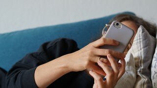 Eine junge Frau liegt auf einem Sofa und schaut auf ihr Handy