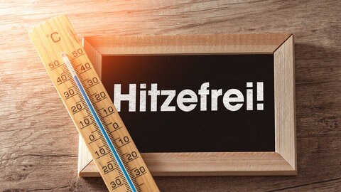 Auf einer Tafel steht "Hitzefrei". Daneben liegt ein Thermometer.