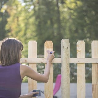 Frau streicht Gartenzaun