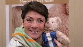 Sonja Faber-Schrecklein lächelt in die Kamera und hält ihren Kuscheltier-Bären an ihre Backe.