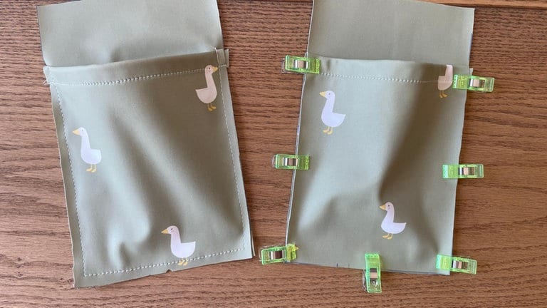 Taschenteile danach auf Oberstoff-Seitenteile stecken, von unten beginnend und seitlich dann die Schnittteile aufeinander legen, sodass die Taschenteile sich wölben. Rundherum mit großem Stich festnähen. 