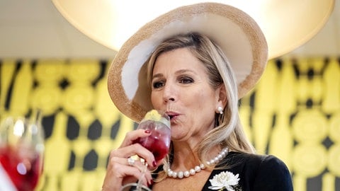 Königin Máxima probiert einen Cocktail während der Eröffnung des 75-jährigen Jubiläums der Hotelfachschule Maastricht und trägt einen Basthut.