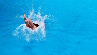 Ein Mann springt ins Becken eines Schwimmbades - im April öffnen die ersten Freibäder in Rheinland-Pfalz (Symbolbild).