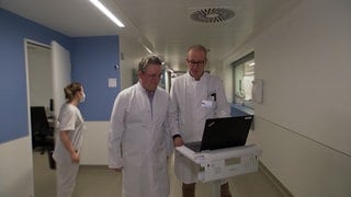 Christian-Friedrich Jehn vom Marienhospital (l.) und Gerald Illerhaus vom Klinikum Stuttgart laufen im Krankenhaus zusammen über einen Flur. Die beiden Kliniken arbeiten seit dem Jahr 2025 im Kampf gegen den Blutkrebs zusammen.