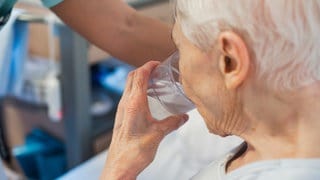 Eine alte Frau trinkt aus einem Glas Wasser. 