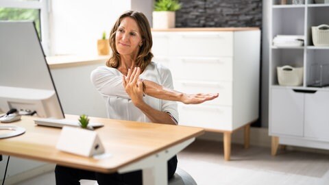 Frau sitzt am Schreibtisch und macht eine Fitnessübung