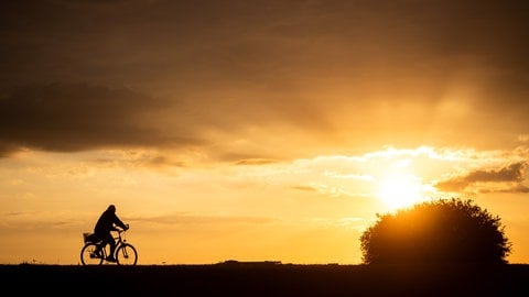 Ein Fahrradfahrer fährt bei Sonnenaufgang über einen Feldweg.