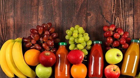 Bananen, Äpfel und Weintrauben liegen mit Fruchtsäften auf einem Holztisch | Gesund leben mit den richtigen Vitaminen: Die Vitamine von A bis E im Überblick