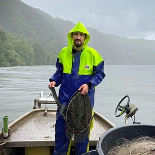 Mann in Regenjacke auf einem Boot vor Bergen.