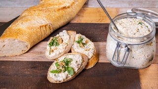 Aufstrich aus Gemüse, Hirse und Frischkäse ist in einem Glasgefäß und lecker angerichtet auf einem Baguette.