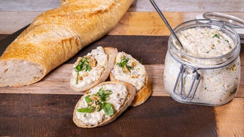 Aufstrich aus Gemüse, Hirse und Frischkäse ist in einem Glasgefäß und lecker angerichtet auf einem Baguette.
