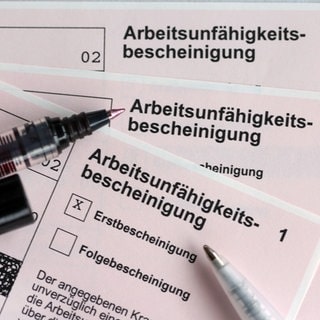Stifte liegen auf den Arbeitsunfähigkeitsbescheinigungen für Arbeitnehmer im Falle einer Krankschreibung durch den Arzt.