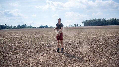 Ulf Allhoff-Cramer steht auf seinem Feld und lässt staubtrockene Erde durch seine Finger rieseln.