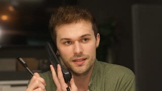 Azubi Kevin sitzt in einem dunklen Raum und hält einen Telefonhörer an sein Ohr.