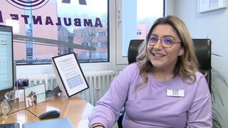 Junge Frau mit lila Pullover und eckiger Brille schaut an der Kamera vorbei. 