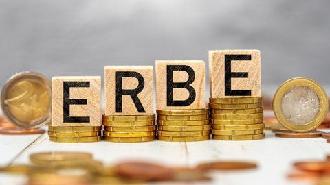 Was können wir zu Lebzeiten schon tun, um unseren Nachlass und unser (digitales) Erbe zu regeln? Testament, Vollmachten, Passwörter sichern - das solltet ihr beachten. Wir geben euch in unserem Ratgeber wichtige Tipps. Das Bild zeigt den Schriftzug "Erbe" auf Holzwürfeln die auf gestapelten Geldmünzen stehen 
