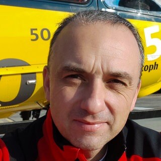 Andreas Bauer steht vor dem Rettungshubschrauber Christoph 22. Auf seinem Ärmel ist das Abzeichen der Crew zu sehen.