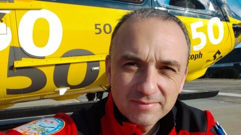 Andreas Bauer steht vor dem Rettungshubschrauber Christoph 22. Auf seinem Ärmel ist das Abzeichen der Crew zu sehen.