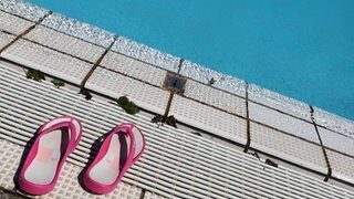 Rosa Flipflops stehen am Beckenrand eines Bades. In mehreren Freibädern wurden Mädchen belästigt. 