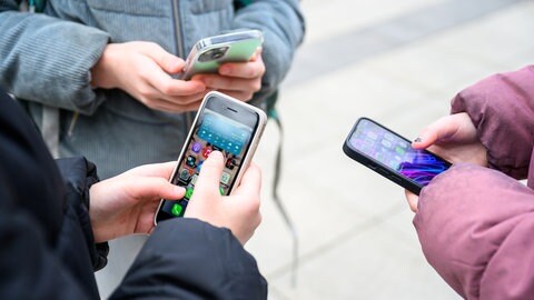 Drei Schüler stehen mit ihren Handys im Pausenhof. Schulen sollen künftig klare Regeln erstellen, wo Smartphones und Co. benutzt werden dürfen.  