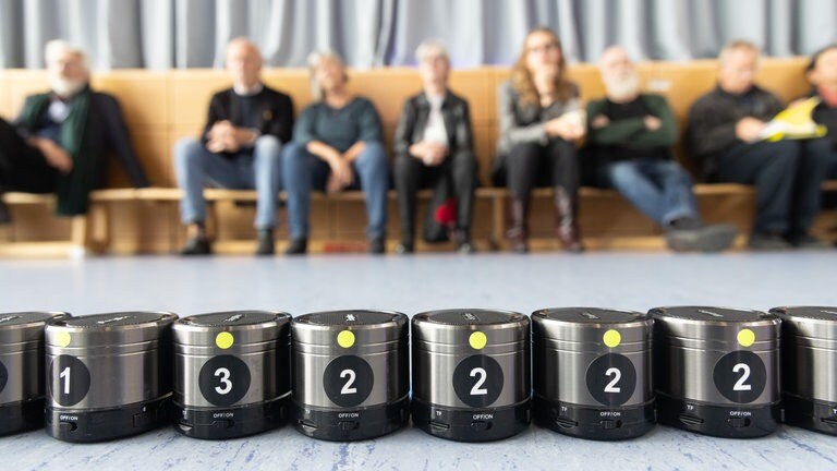 Reihe von Minilautsprechern, dahinter Reihe von sitzenden Menschen