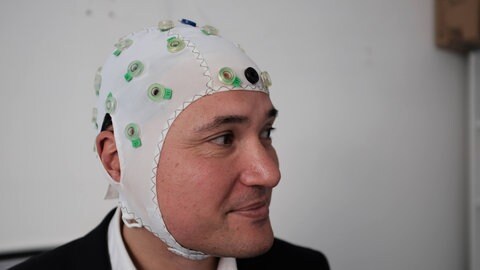 Prof. Surjo Soekadar mit einer Haube zur Messung von Hirnströmen. Zu ihm an die Charité Berin kommen Menschen, die eine schwere Depression haben oder von Wahnvorstellungen heimgesucht werden, oft verbunden mit eindringlichen Stimmen. 