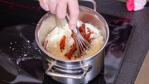 Die Sahnesauce für den Chicorée wird in einem Topf zubereitet. Zur Sahne kommen Tomaten und Käse hinzu. 